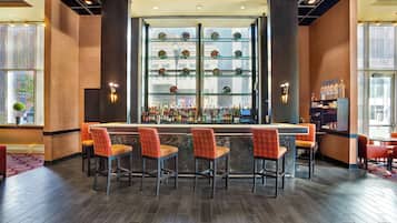 A bar area with a long counter, multiple shelves of bottles, and four bar stools.