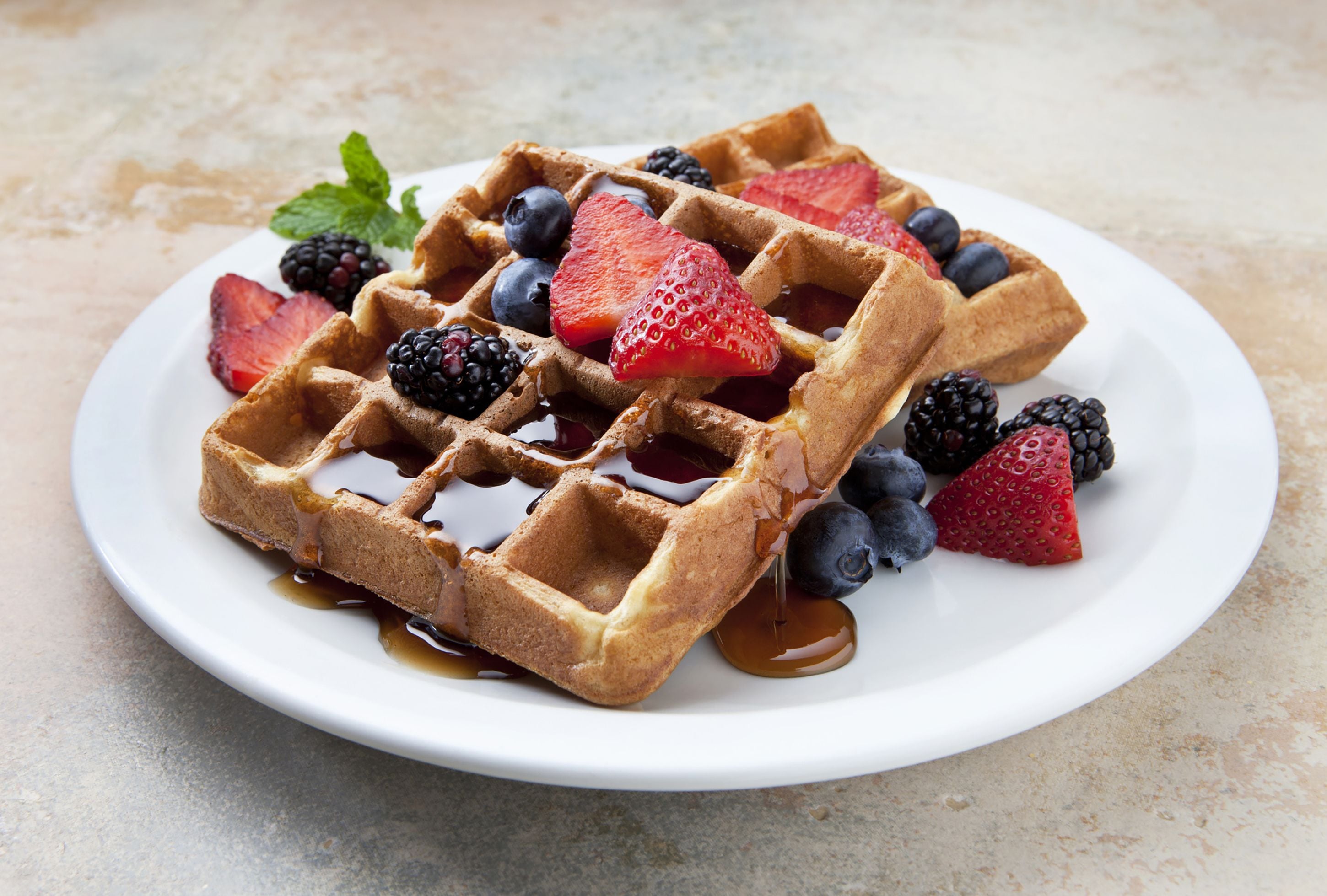 A plate of waffles with syrup and fresh berries.