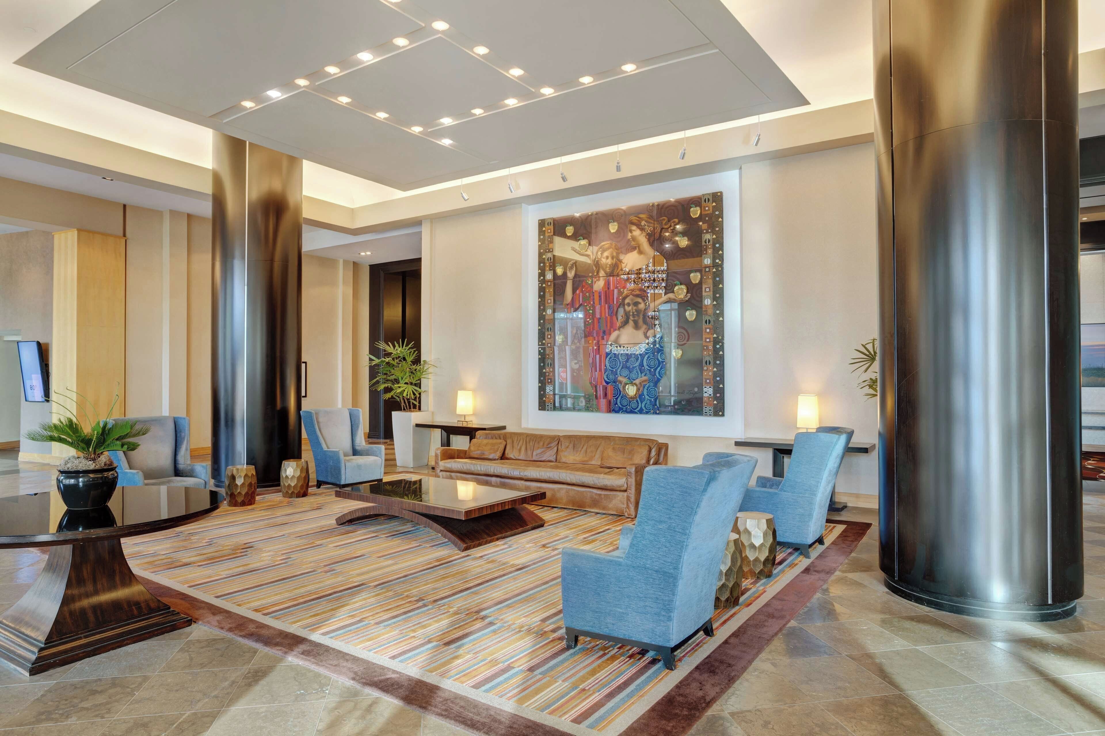A modern lobby with a large abstract painting, a seating area with sofas and chairs, and a large metallic column.