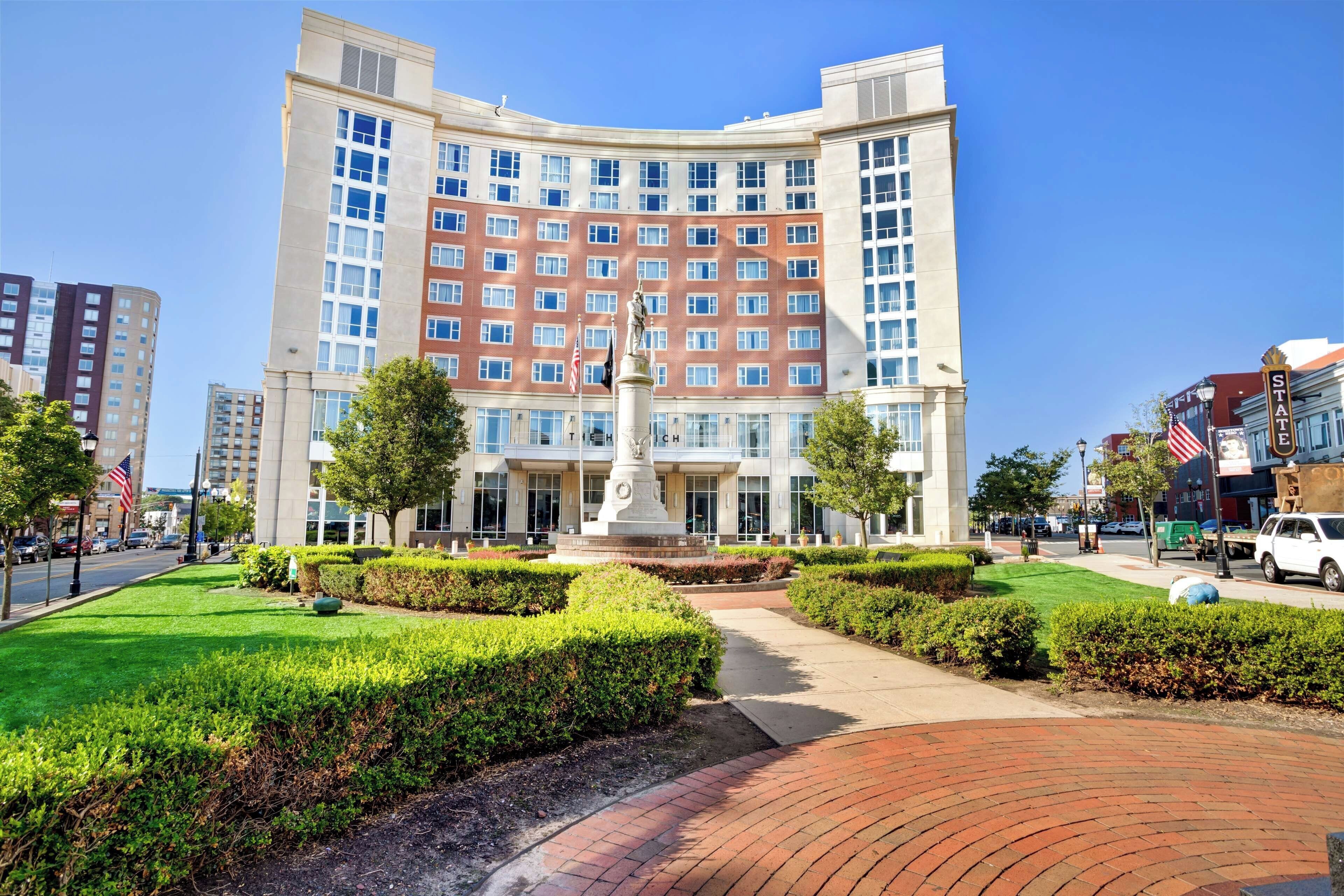 A multi-story hotel with a central courtyard, a statue, and a flag.