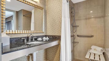 A modern bathroom with a granite countertop, a large mirror, a shower with a handheld showerhead, and a towel rack.