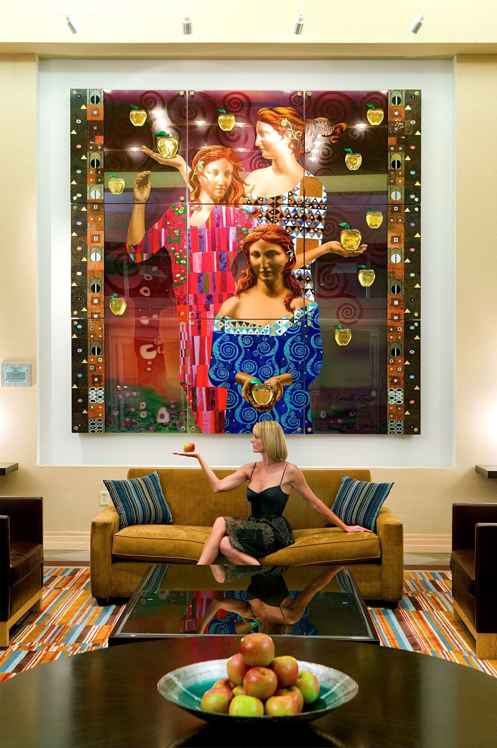 A woman sitting on a sofa in front of a colorful abstract painting.