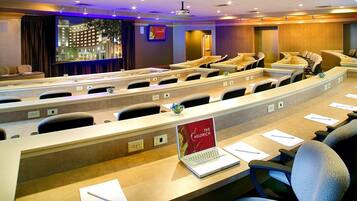 A conference room with rows of tables and chairs, a projector screen, and a laptop on one table.