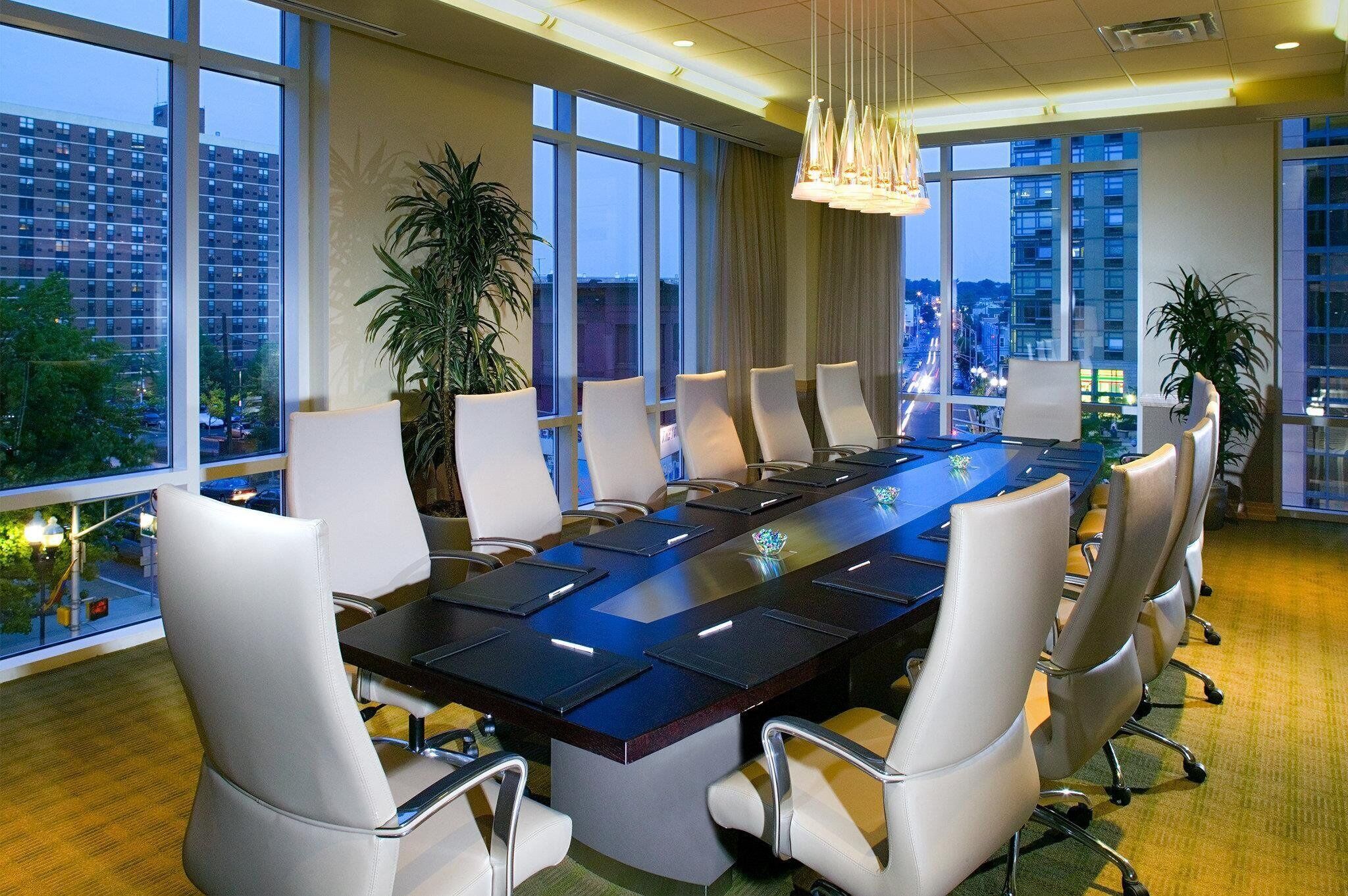 Une salle de conférence dotée d’une longue table, de chaises blanches et de grandes fenêtres offrant une vue sur la ville.