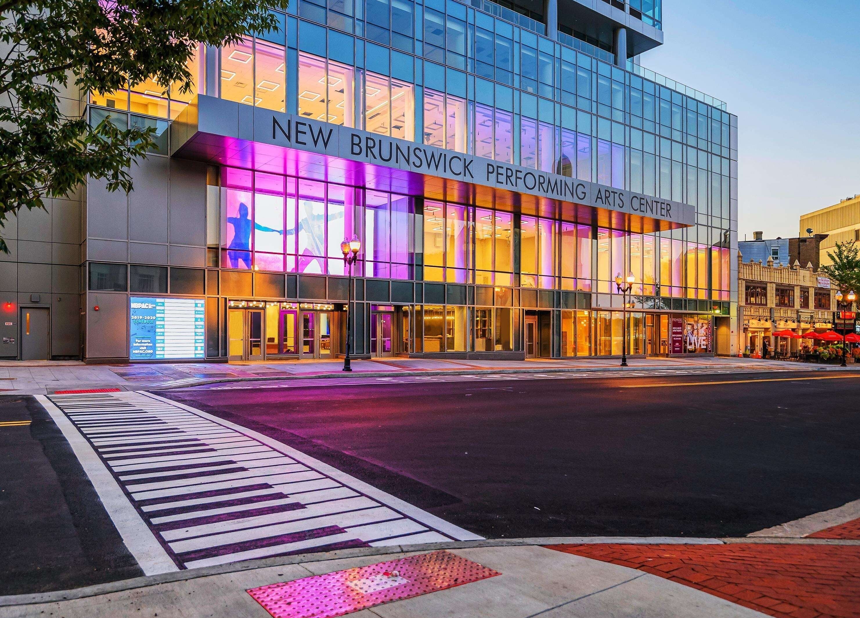 The exterior of the New Brunswick Performing Arts Center with a modern glass facade and illuminated signage.