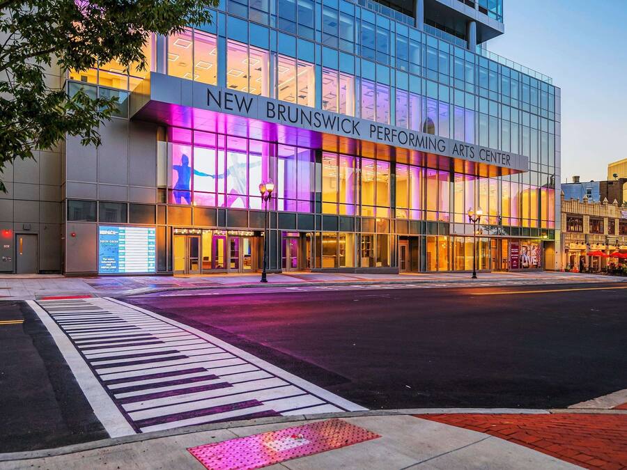 The exterior of the New Brunswick Performing Arts Center with a modern glass facade and illuminated signage.