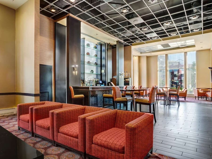 A hotel lobby with a bar area, seating arrangements, and a view through large windows.