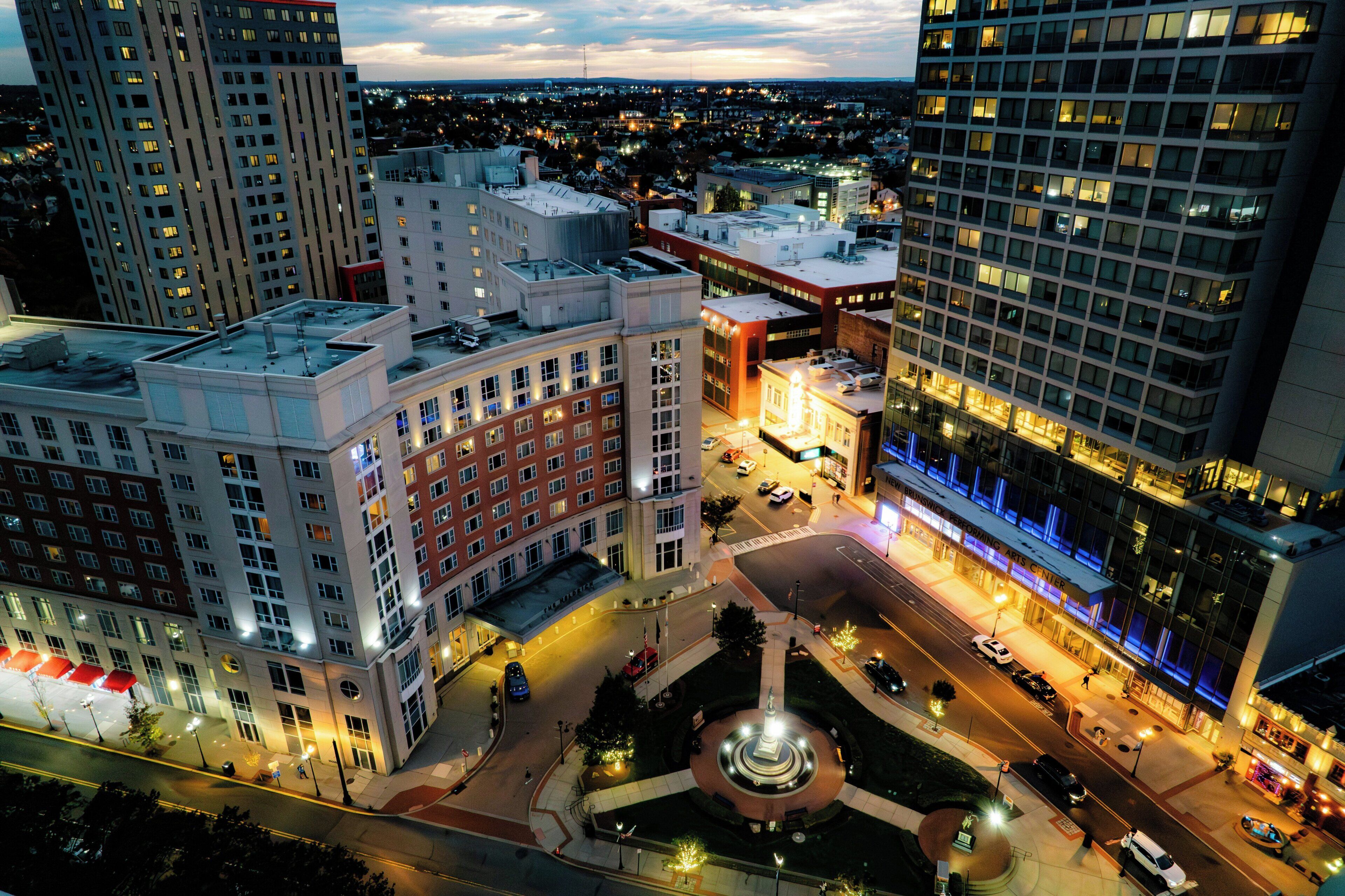 A cityscape with a prominent building featuring a central plaza with a fountain, surrounded by high-rise buildings.