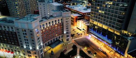A cityscape with a prominent building featuring a central plaza with a fountain, surrounded by high-rise buildings.