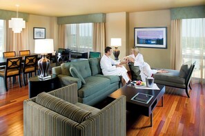 A hotel room with a green sofa, a dining table with chairs, a TV, and a cityscape view. - The Heldrich Hotel (New Brunswick)