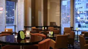 Un hall d’hôtel avec des tables rondes, des fauteuils confortables et de grandes fenêtres donnant sur le paysage urbain.
