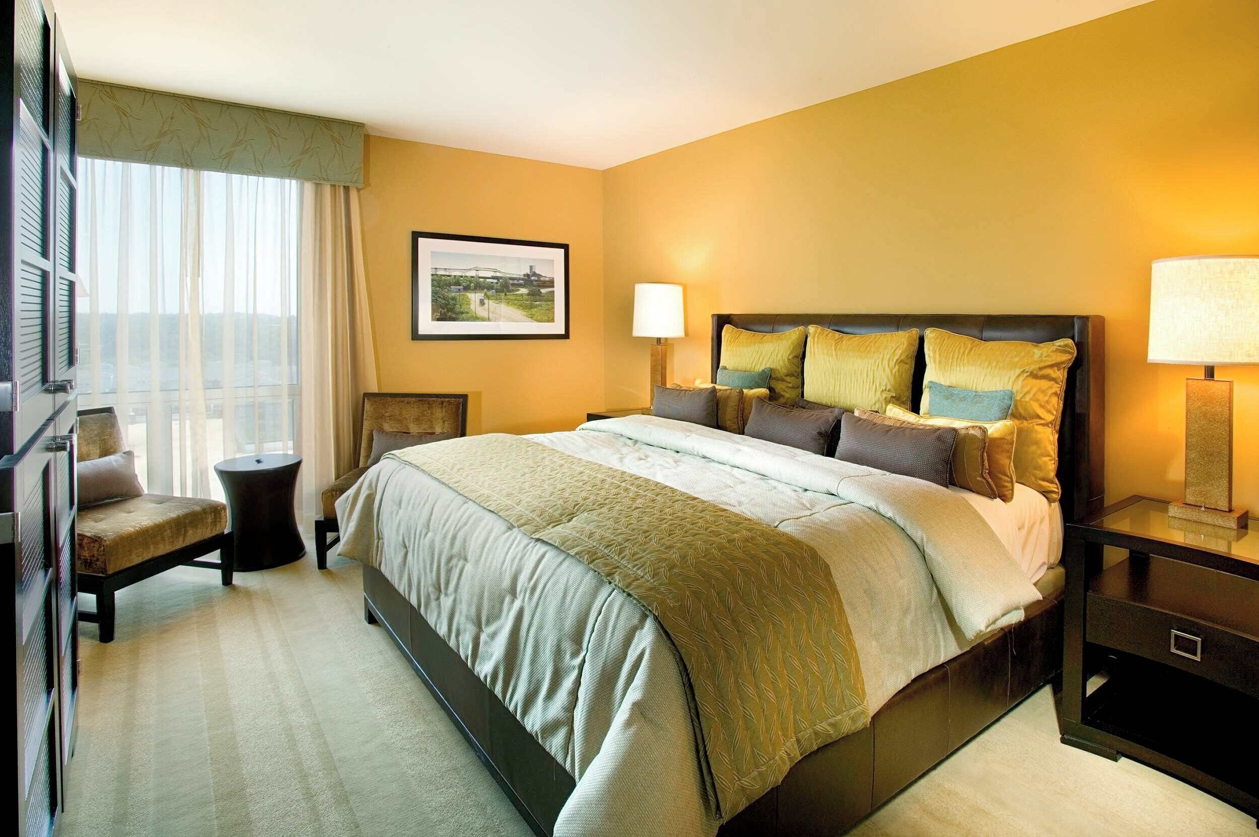 A hotel room with a large bed, a chair, a desk, and a window with curtains.