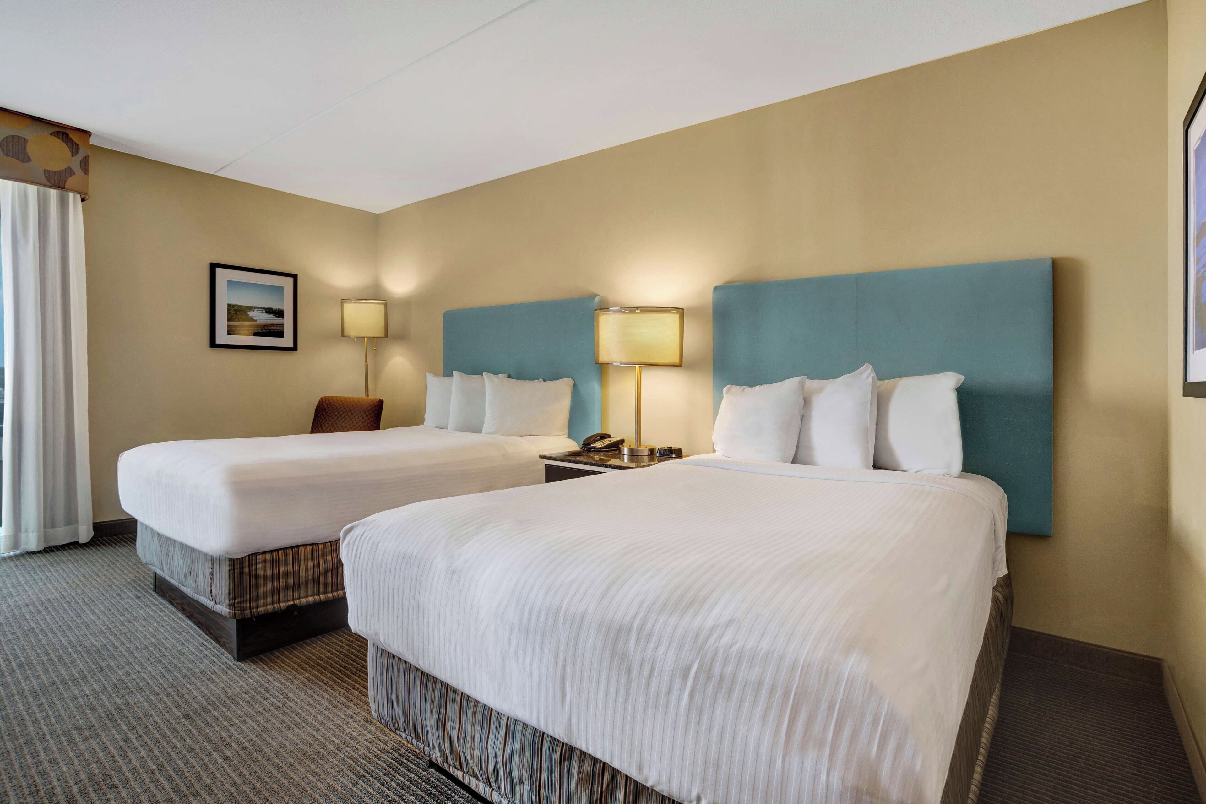 Habitación de hotel con dos camas, una mesita de noche con lámpara y un cuadro en la pared.
