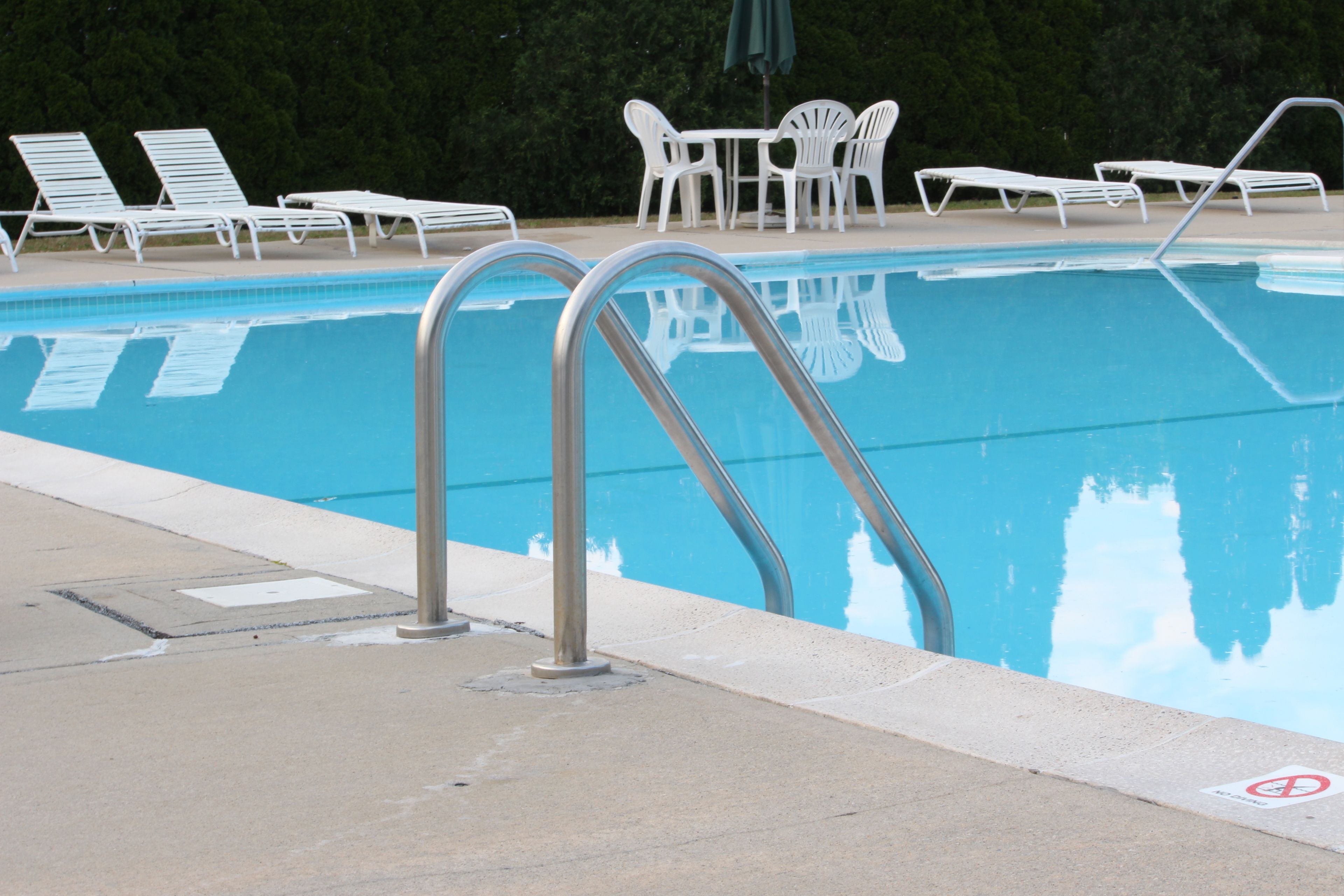 A swimming pool with metal ladders, white lounge chairs, and a table with chairs.