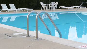 A swimming pool with metal ladders, white lounge chairs, and a table with chairs.