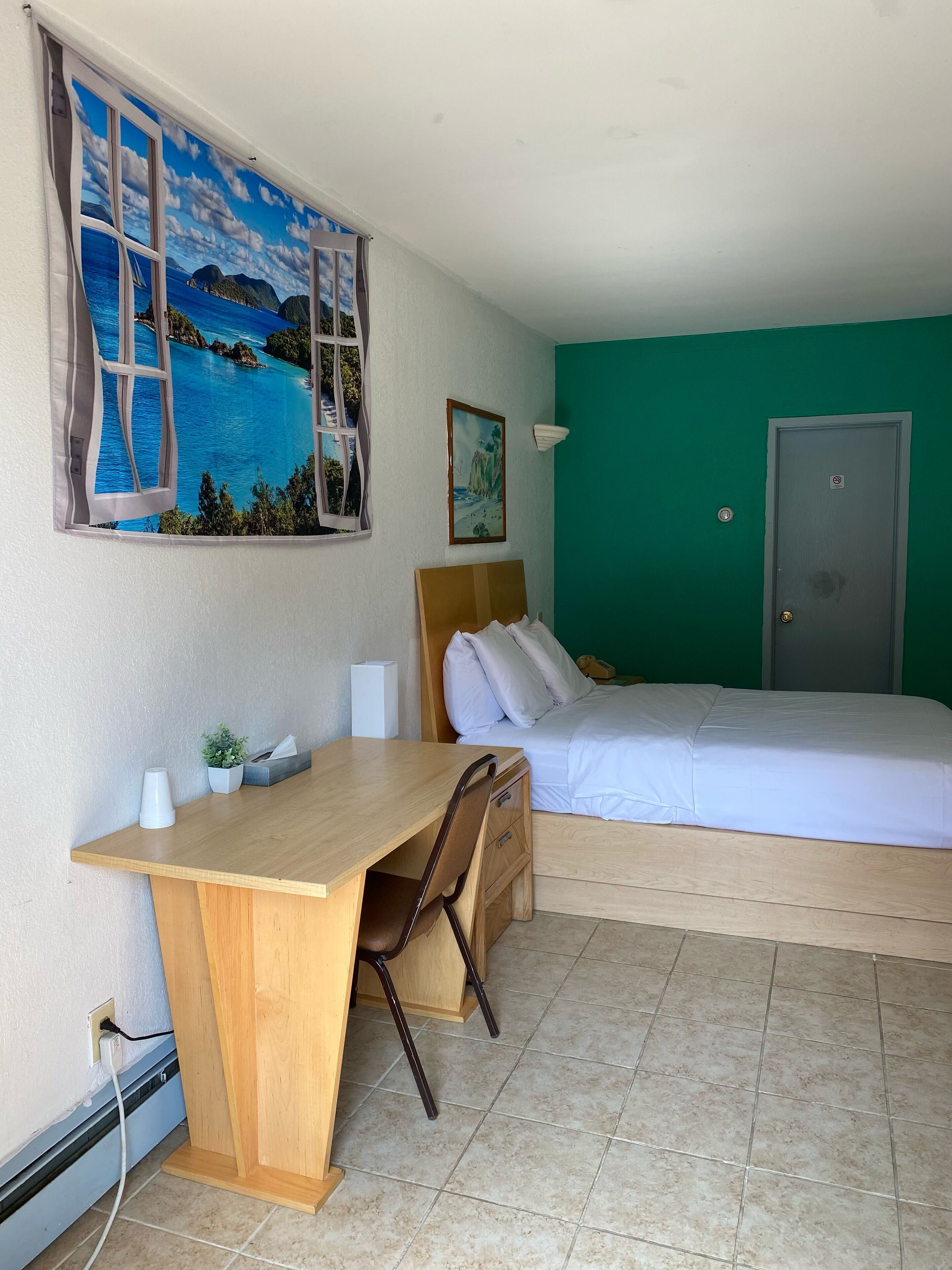 Hotelkamer met een bed, een bureau, een stoel, een raam met uitzicht op zee en een groene wand.