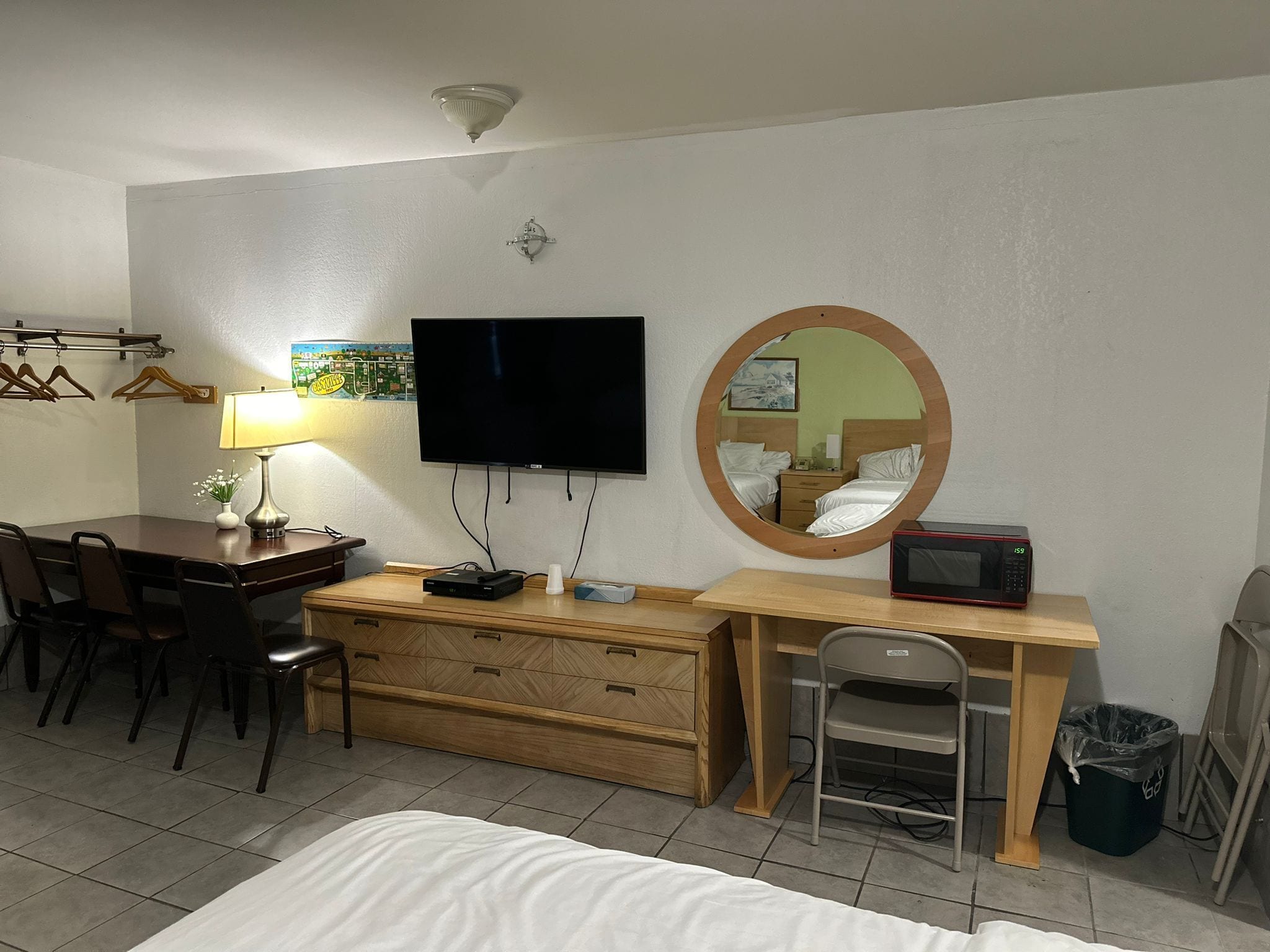 A hotel room with a bed, a desk with a computer, a TV, a mirror, a microwave, and a trash bin.