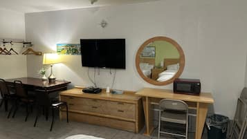 A hotel room with a bed, a desk with a computer, a TV, a mirror, a microwave, and a trash bin.