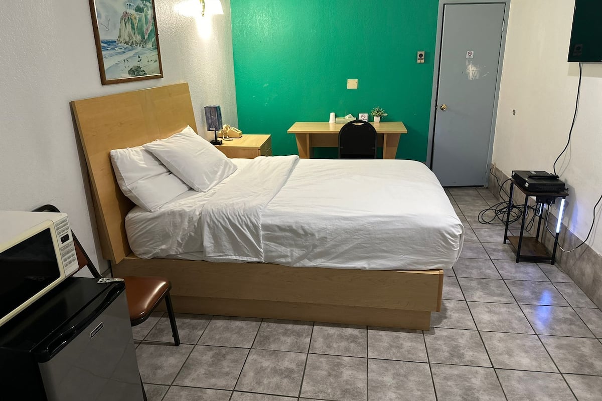 A hotel room with a bed, a desk, a chair, a telephone, and a television.