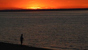 A sunset over a body of water with a silhouette of a person standing on the shore. - Tides Motor Inn at Stehli Beach (Locust Valley)