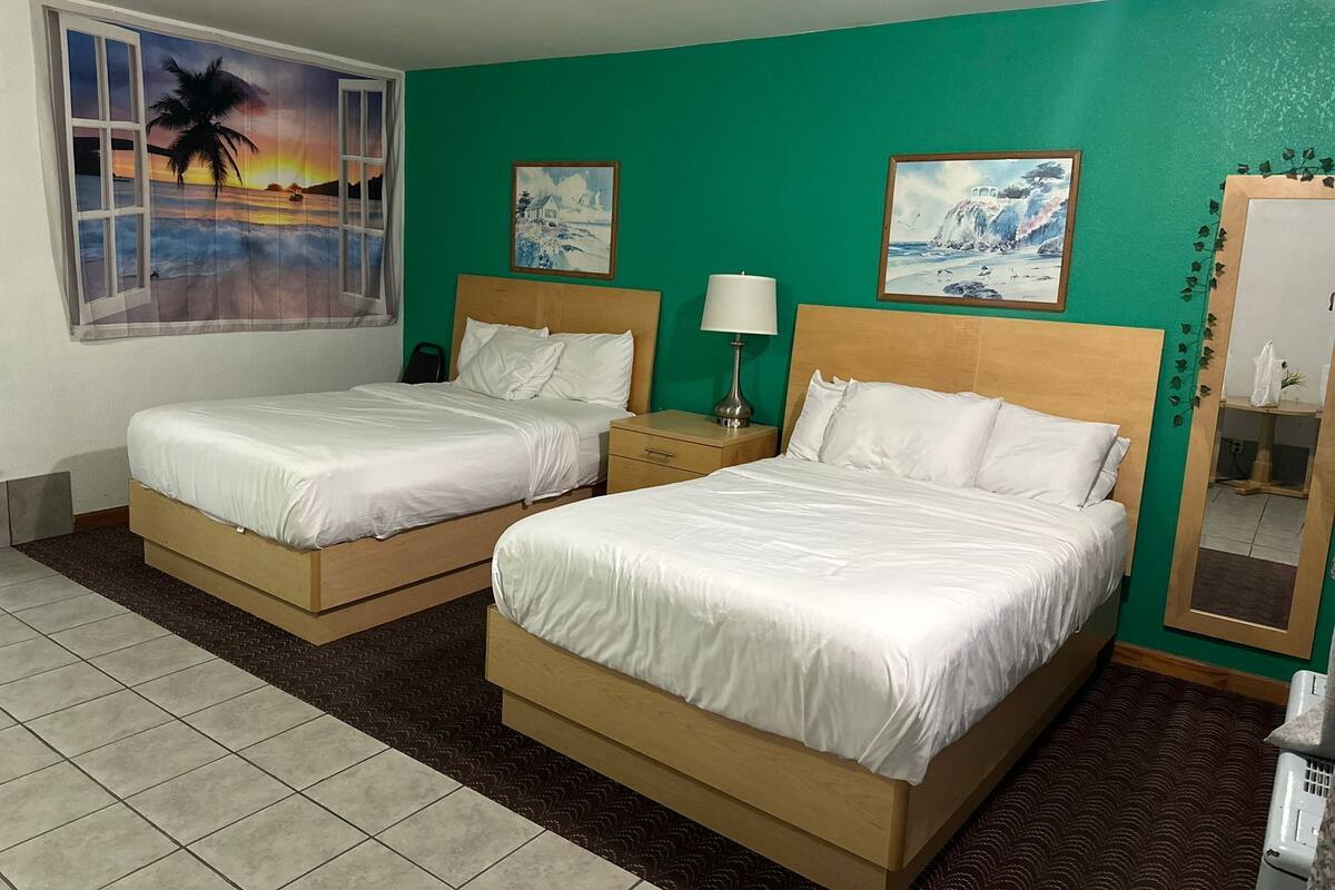 A hotel room with two beds, a window with a sunset view, and green walls.