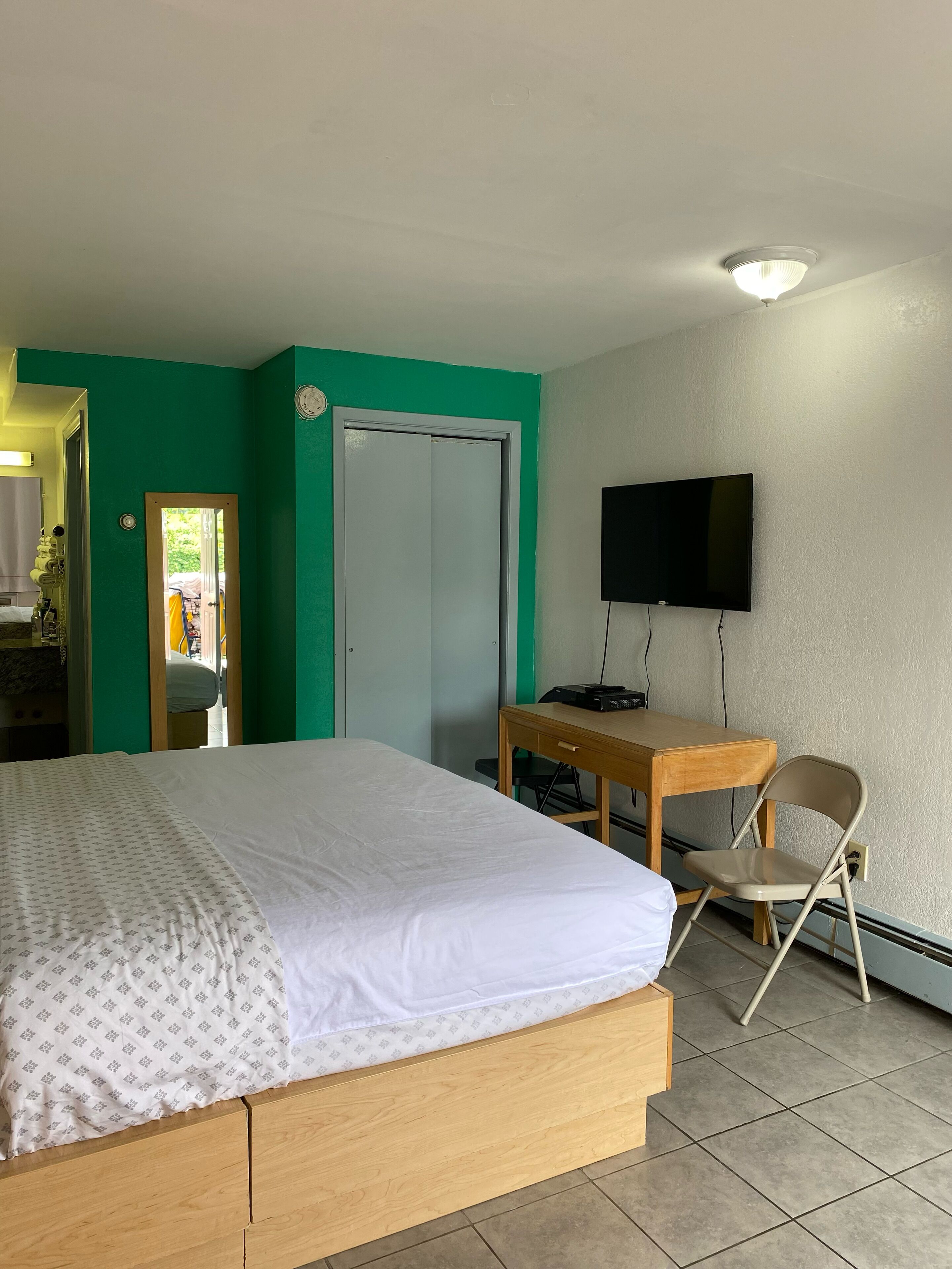 A room with a bed, a desk, a chair, a television, and a door.