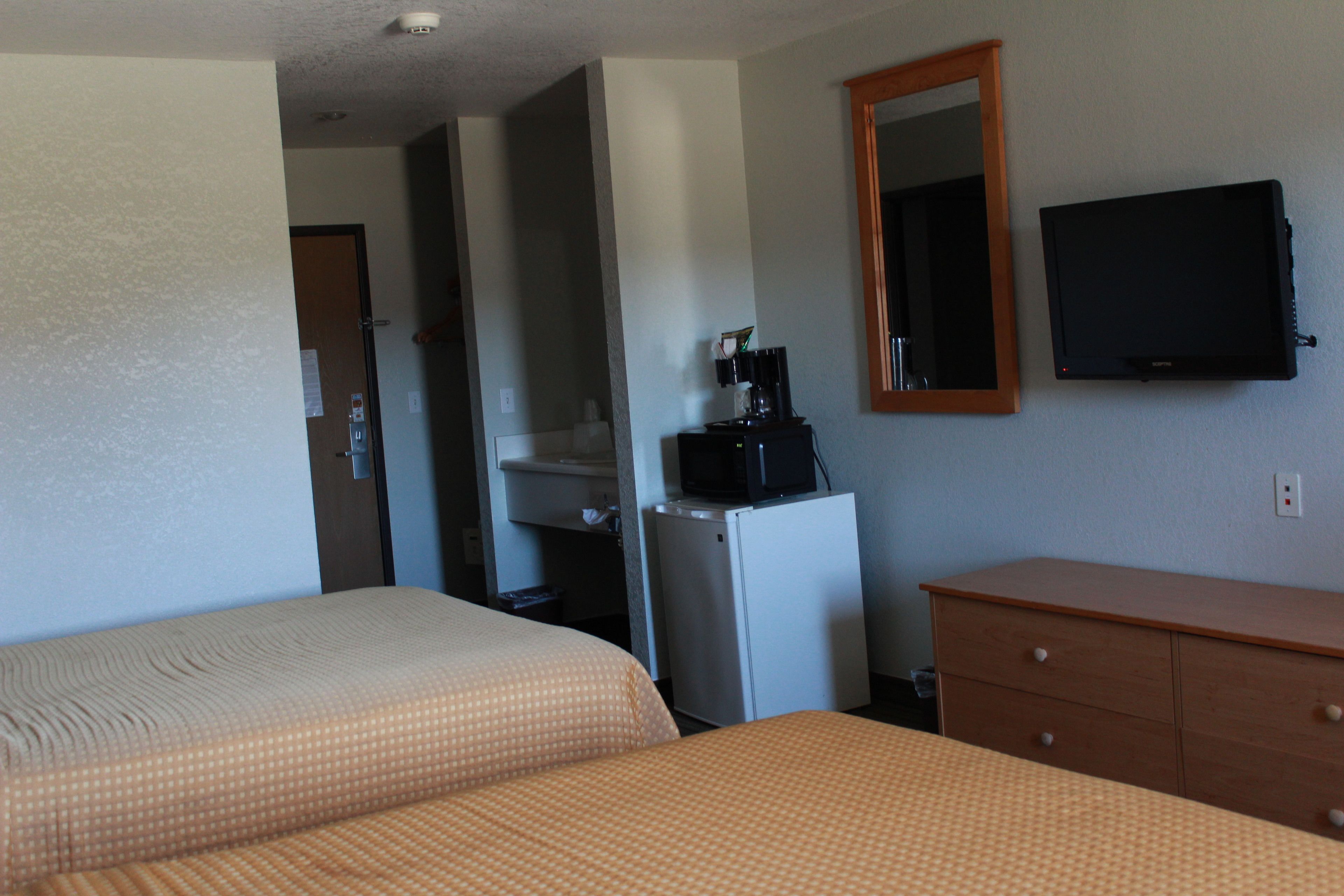 A hotel room with two beds, a small refrigerator, a coffee maker, a television, and a wooden dresser.