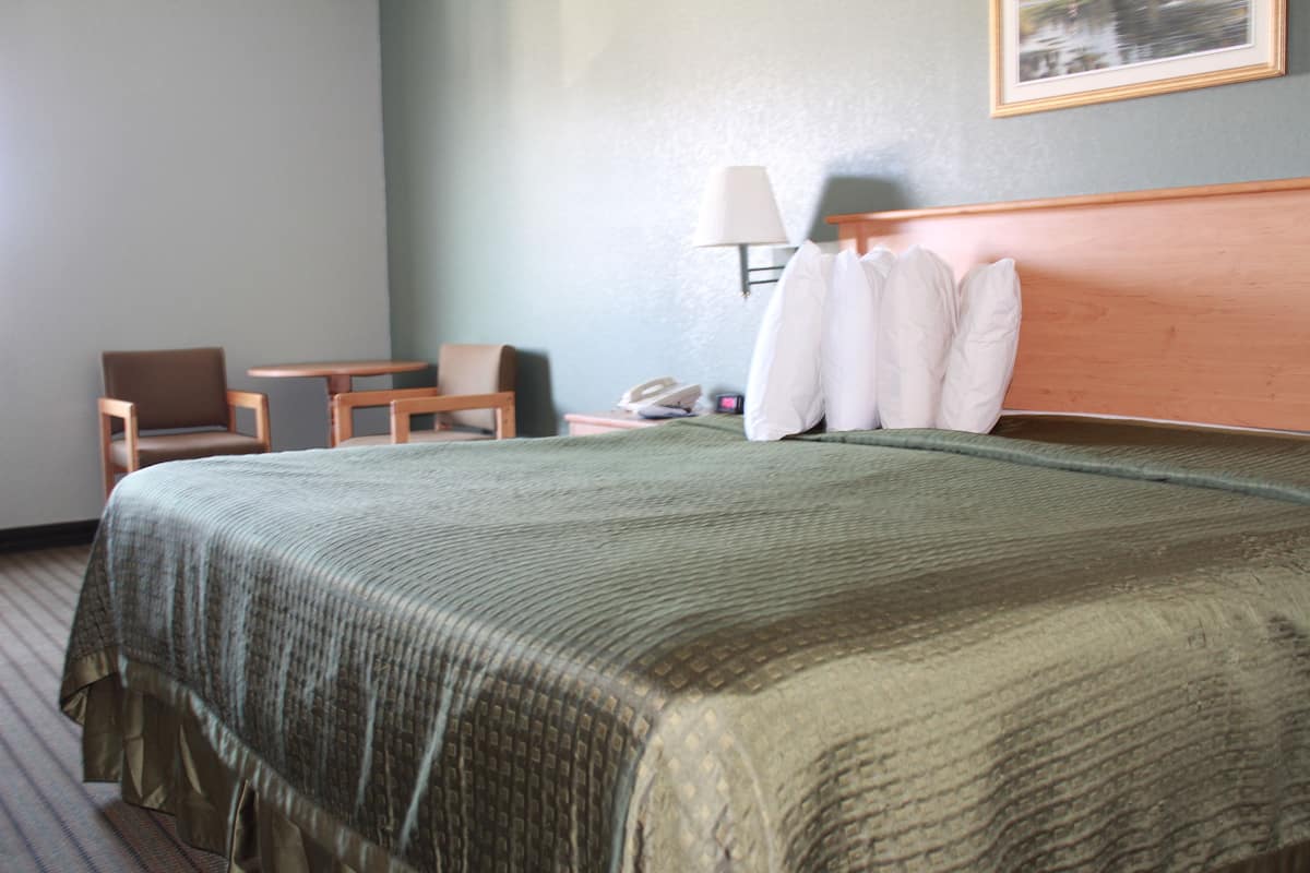 Une chambre d’hôtel avec un lit, une chaise, une petite table, une lampe et un téléphone sur la table de chevet.