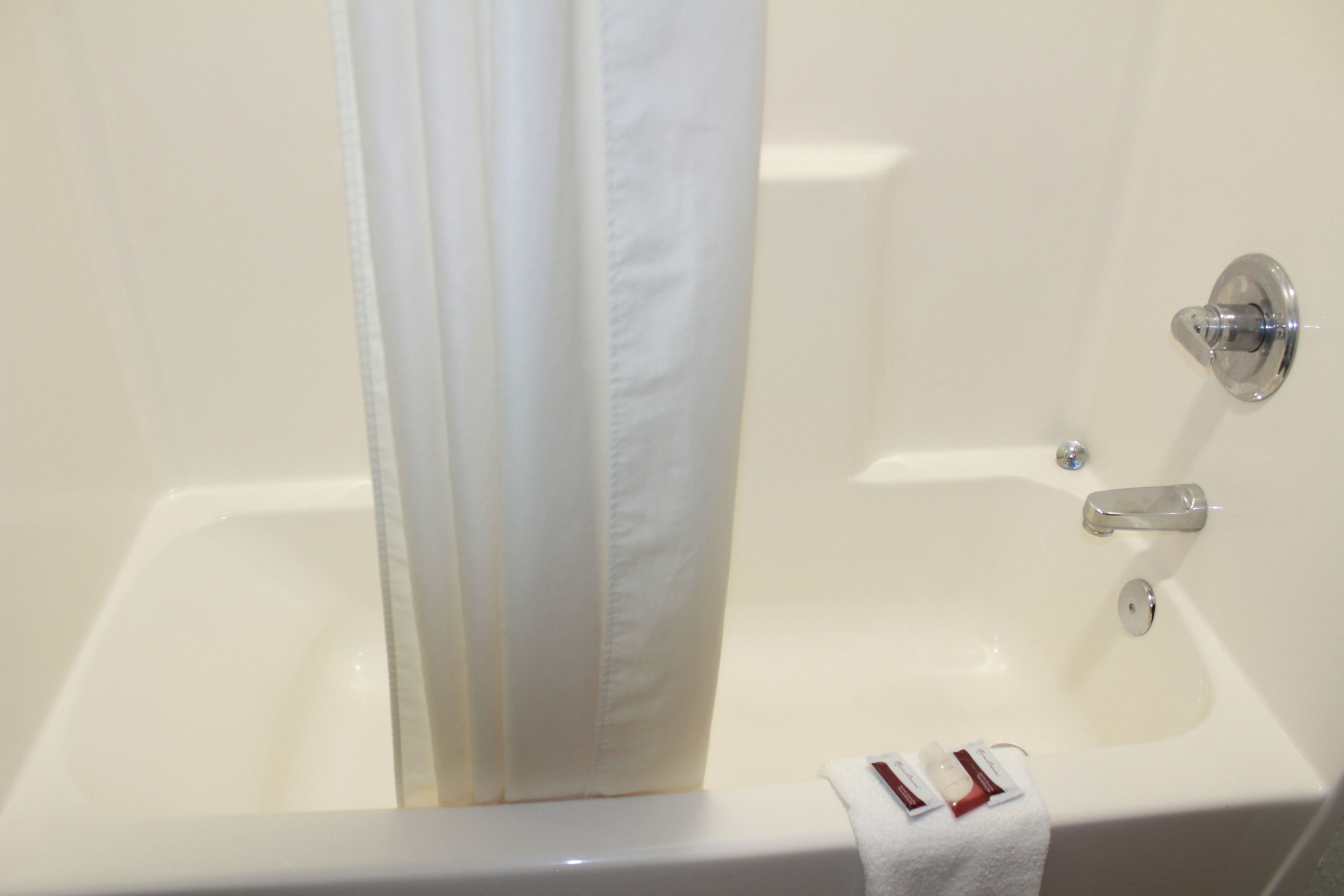 Una bañera blanca con cortina de ducha, una toalla y una botella de champú.