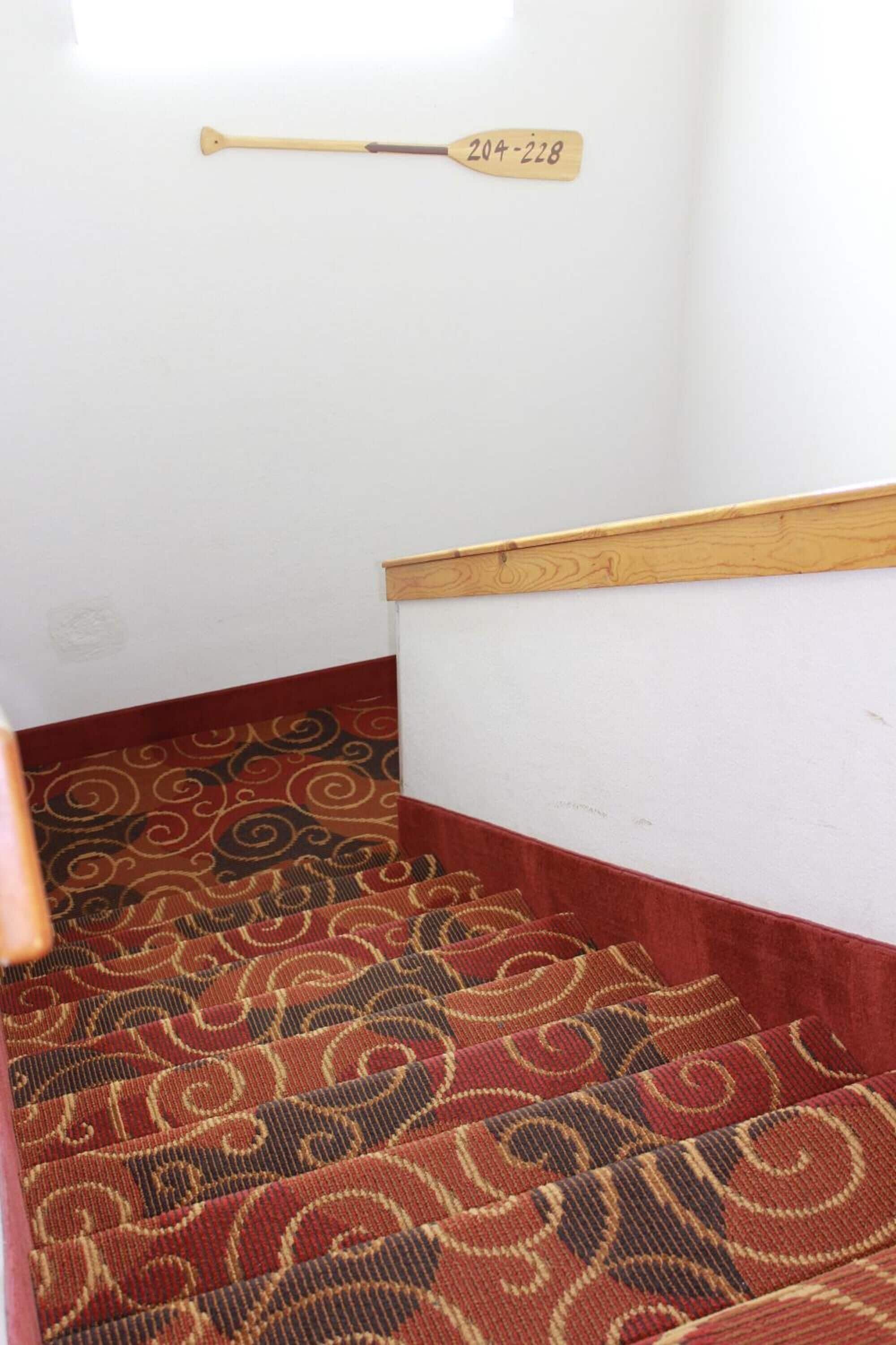 A carpeted staircase with a wooden handrail and a baseball bat hanging on the wall.