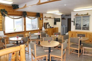 Un restaurante de estilo cabaña acogedor con paredes y muebles de madera, que cuenta con mesas y sillas redondas, una estación de café y un gran ventanal con vistas.