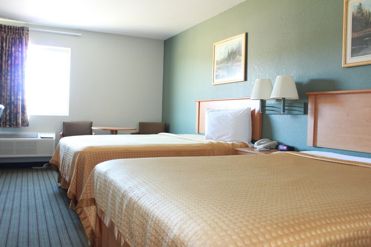 Une chambre d’hôtel avec deux lits, un bureau, une chaise, une lampe et un tableau au mur.