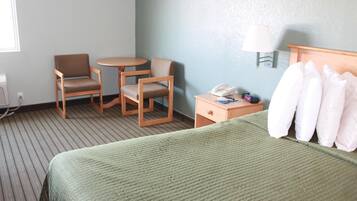 Habitación de hotel con cama, dos sillas, una mesita, una mesita de noche con lámpara y teléfono.