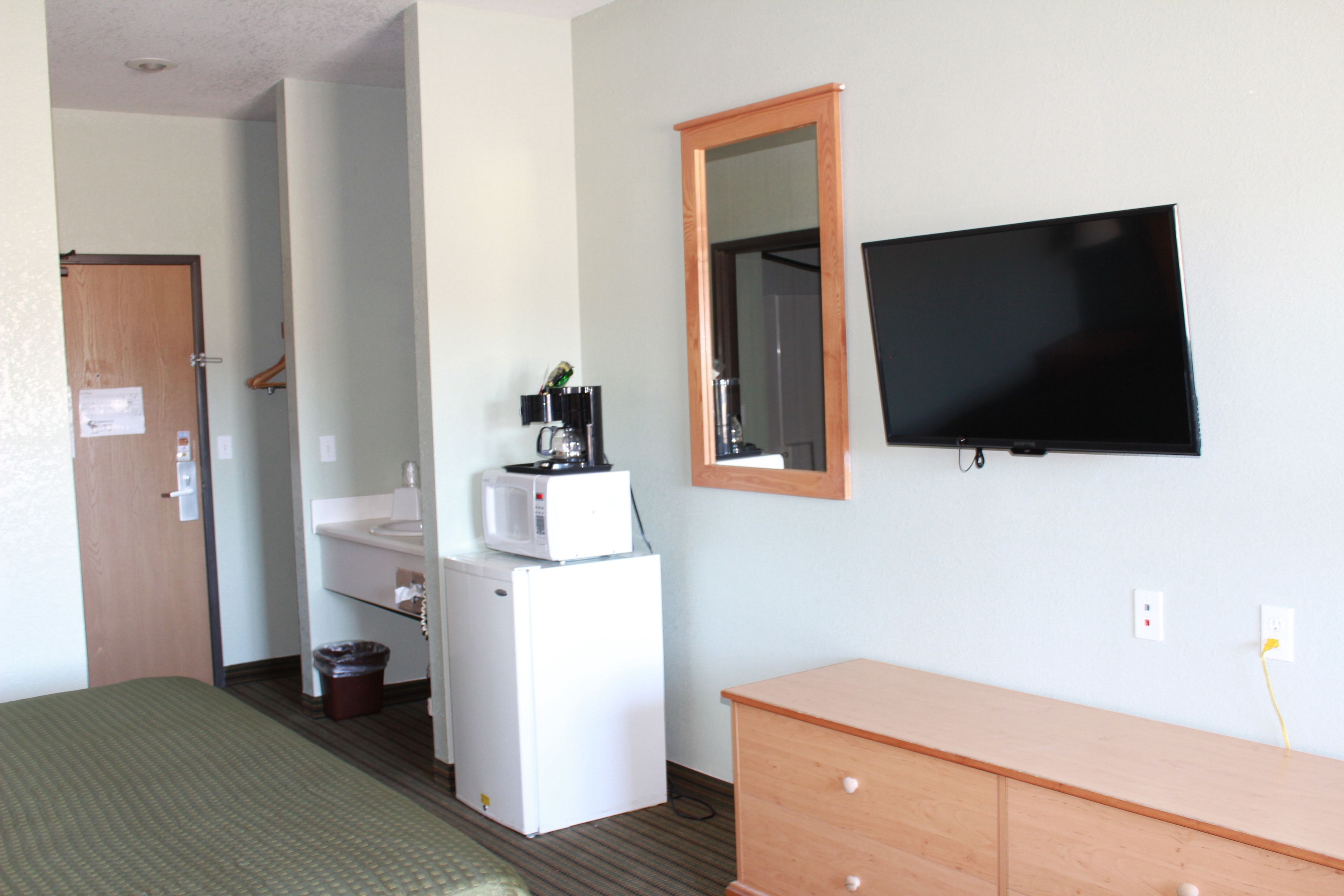 A hotel room with a bed, a wooden dresser, a television, a microwave, a small refrigerator, a sink, and a mirror.