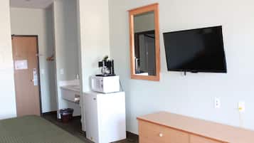 A hotel room with a bed, a wooden dresser, a television, a microwave, a small refrigerator, a sink, and a mirror.