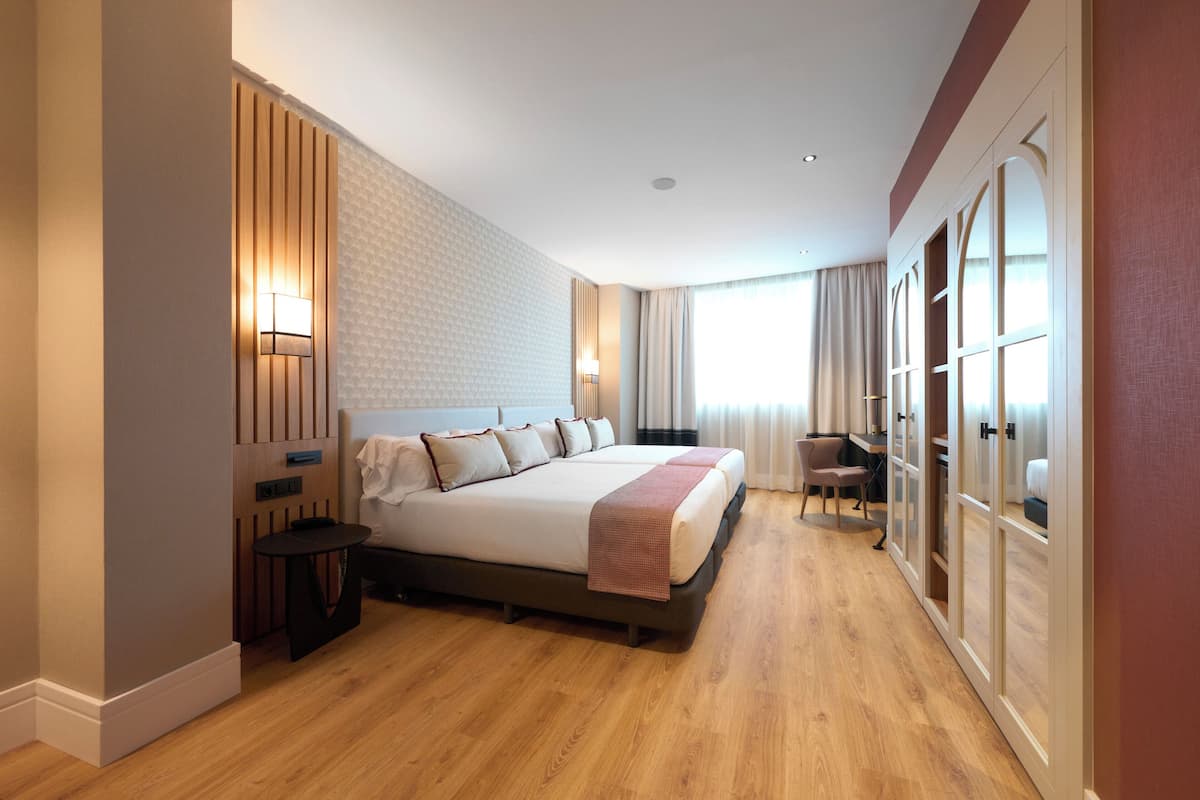A modern hotel room with a large bed, a desk, and a wardrobe.