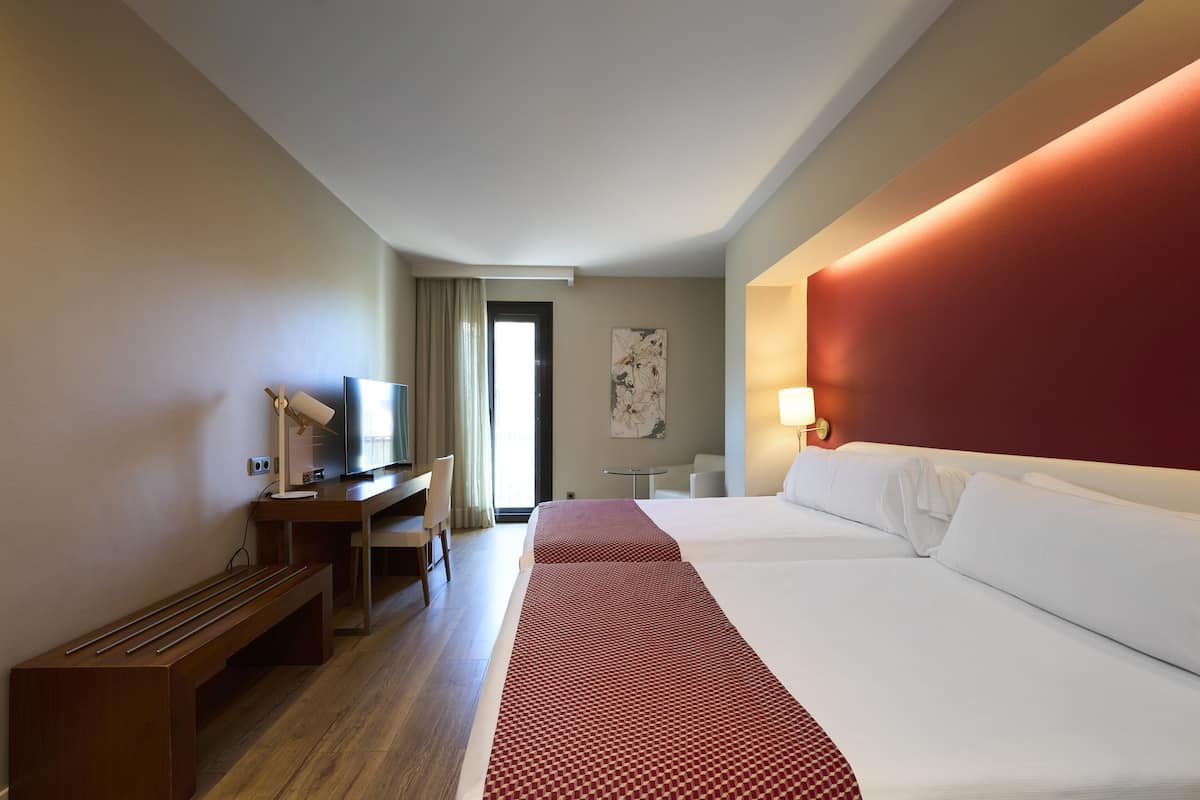 A hotel room with a desk, two beds, a TV, and a window with curtains.