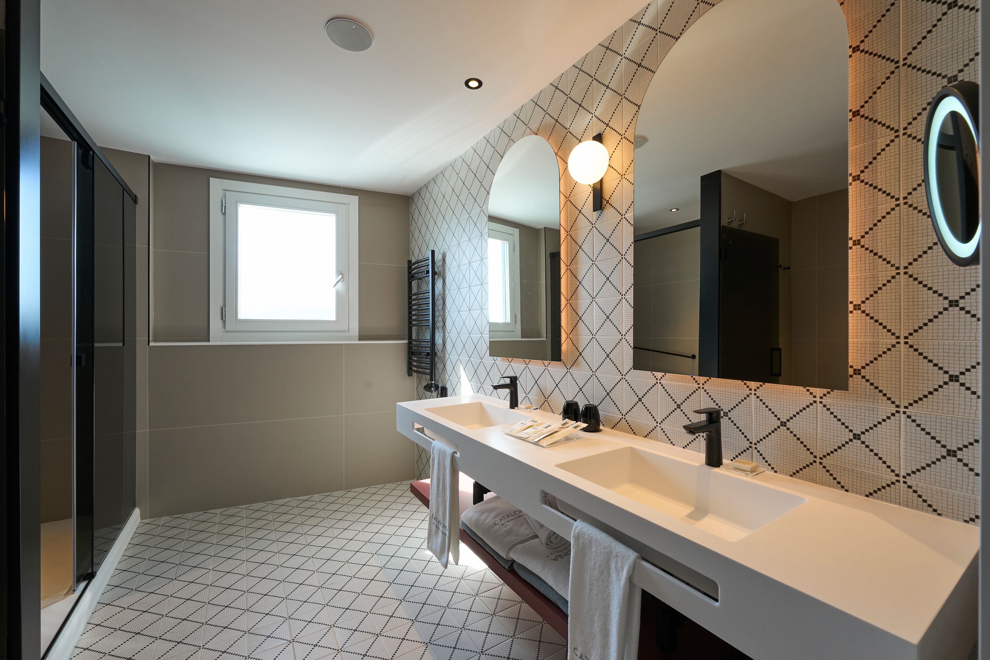 Un baño moderno con dos lavamanos, un espejo grande y un diseño de baldosas geométricas en las paredes.