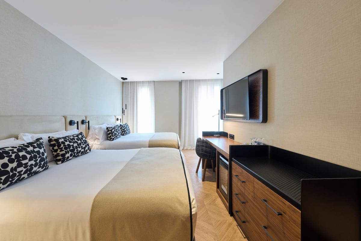 A hotel room with two beds, a desk, a TV, and a minibar.
