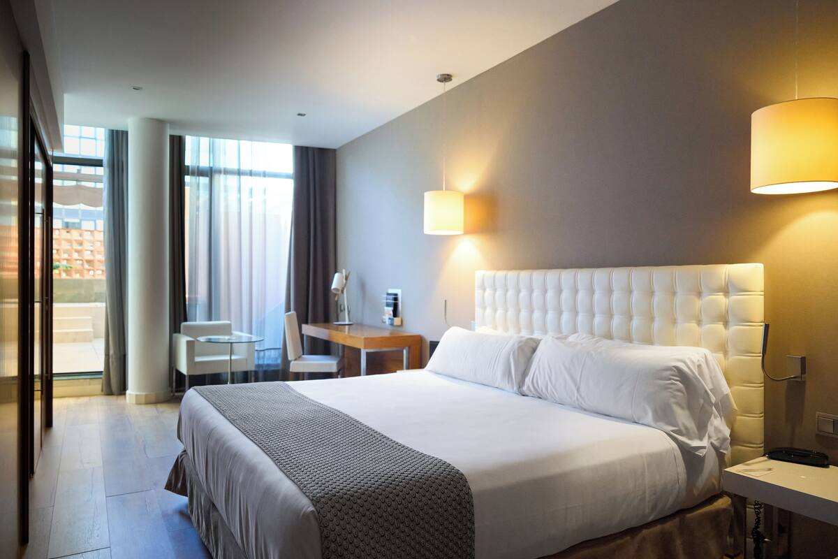 A modern hotel room with a large bed, a desk, and a chair.