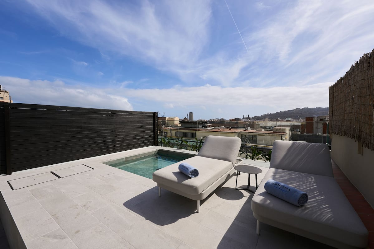 A rooftop terrace with a pool, two lounge chairs, and a small table.