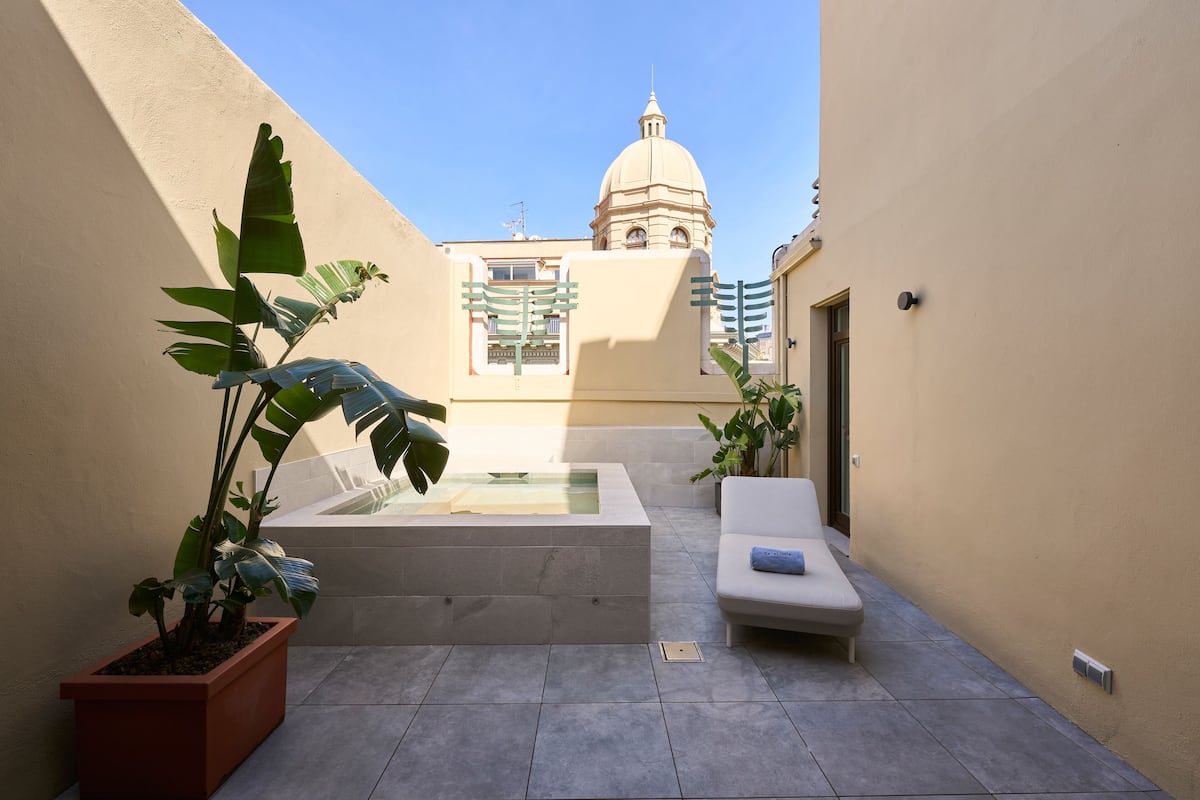 A courtyard with a hot tub, a lounge chair, and potted plants.