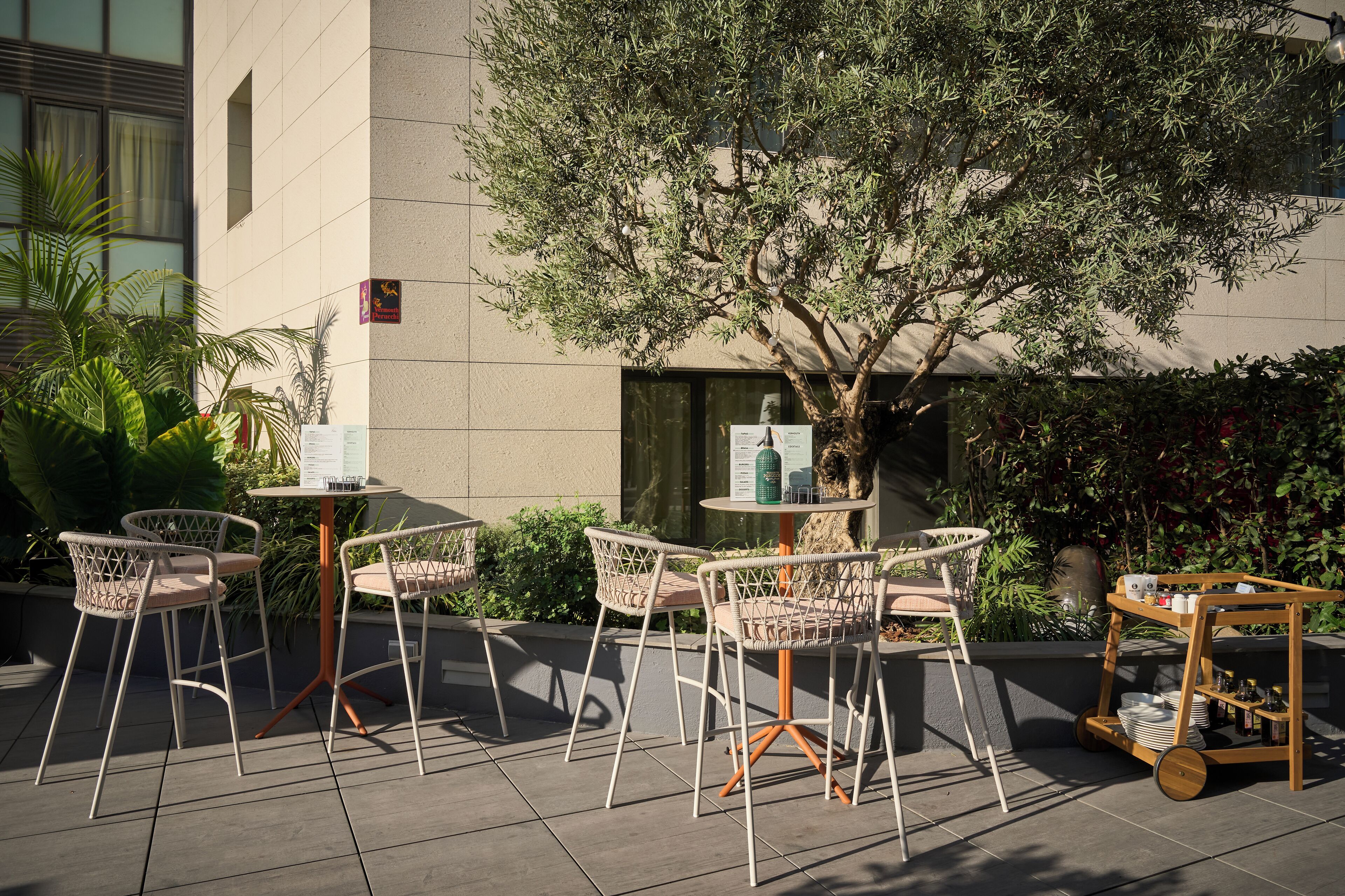 Een terras met rieten stoelen en een tafel, omringd door planten en een boom.