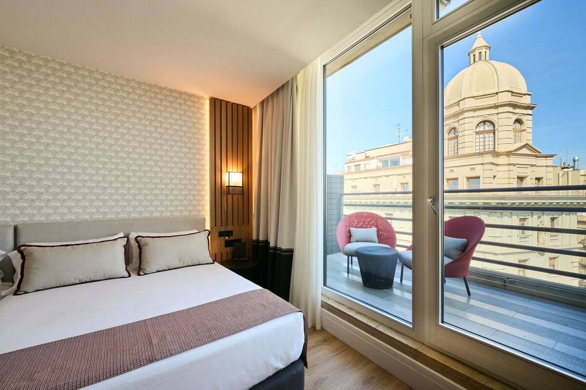 A hotel room with a large bed, a view of a building with a dome, and a balcony with chairs.