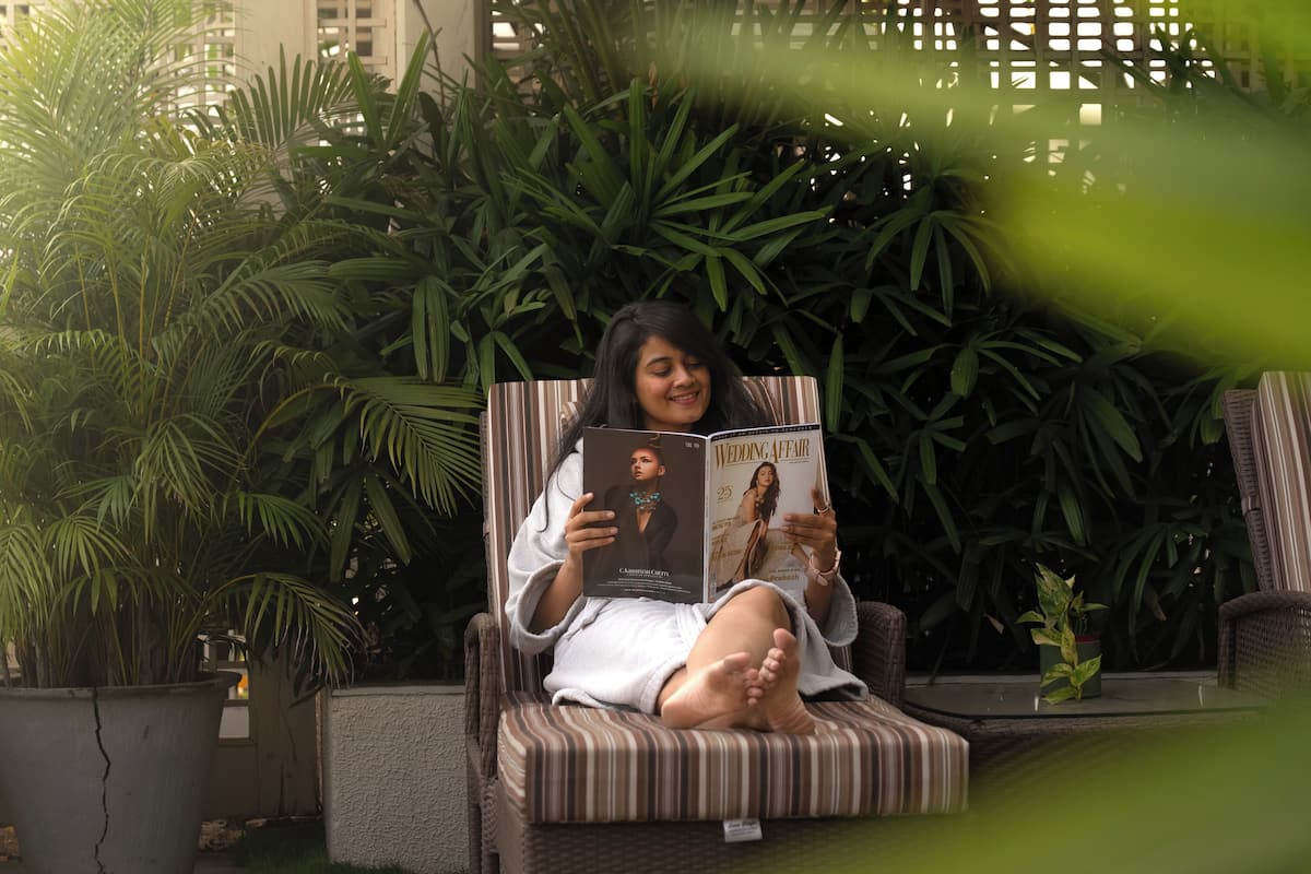 Une personne assise sur une chaise à rayures, en train de lire un magazine.