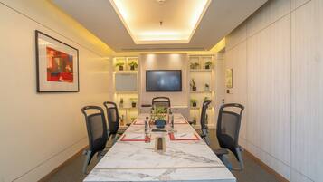 Un salón de conferencias con una larga mesa, sillas, una televisión, estanterías con plantas y un cuadro en la pared.