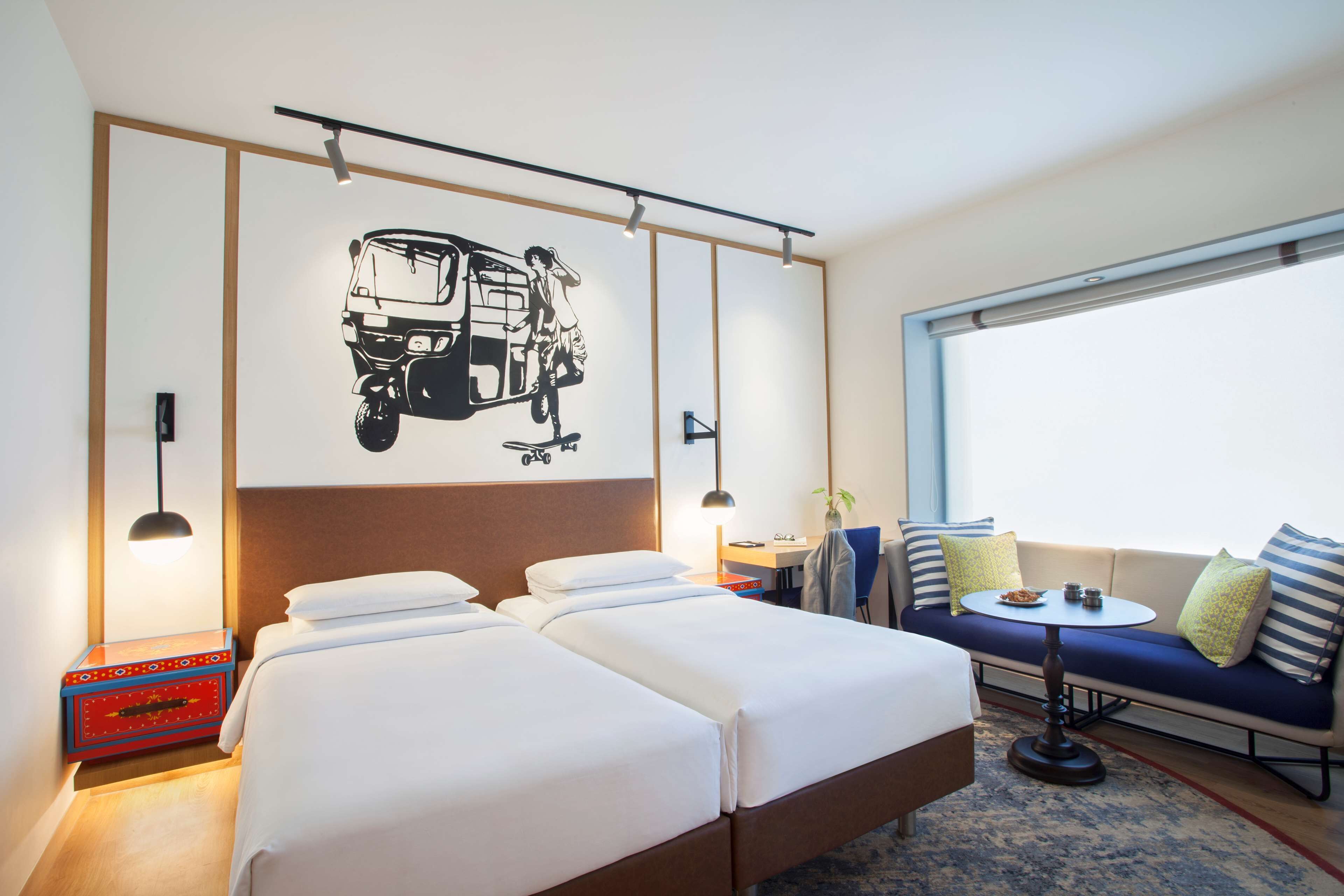 A hotel room with two beds, a sofa, a small table, and a large window.