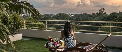 A person relaxing on a lounge chair with a table of food and drinks in front of them, overlooking a lush landscape.