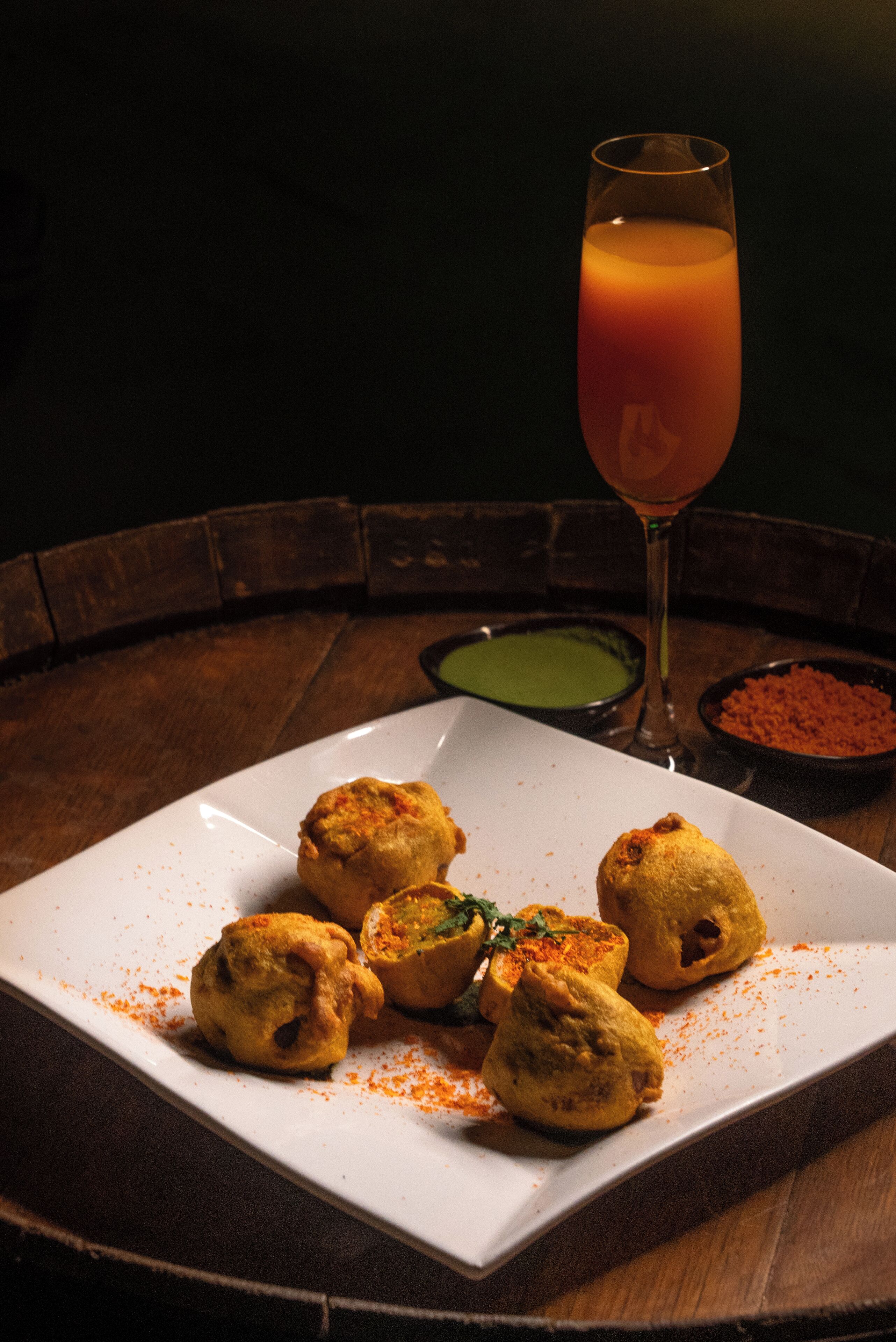A plate of food with a glass of orange juice and two small bowls of sauces on a wooden table.