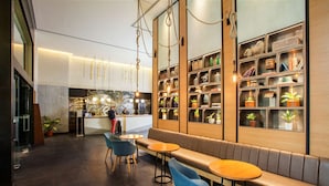 Een modern interieur met een receptiebalie, een zithoek met tafels en stoelen, en een boekenplank met diverse objecten.